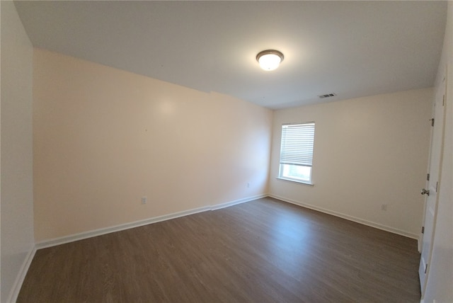 spare room with visible vents, baseboards, and dark wood-style floors