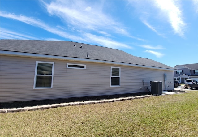 back of property featuring central AC unit, a shingled roof, and a yard