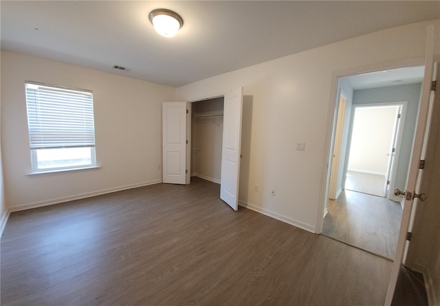 unfurnished bedroom featuring visible vents, baseboards, a closet, and wood finished floors