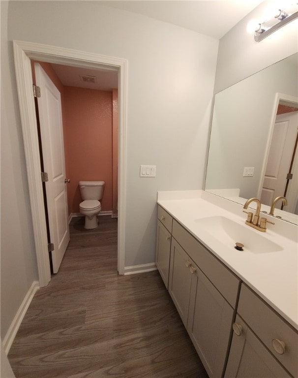 bathroom featuring visible vents, toilet, wood finished floors, baseboards, and vanity