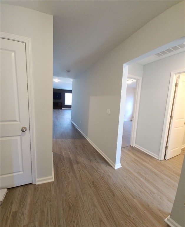 corridor featuring visible vents, baseboards, and wood finished floors