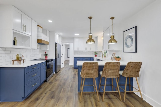 kitchen with pendant lighting, blue cabinetry, premium range hood, stainless steel appliances, and white cabinets