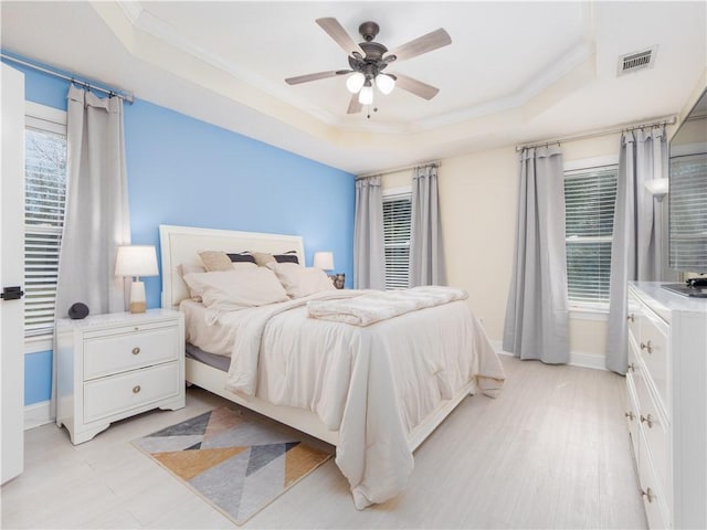 bedroom with ceiling fan, visible vents, baseboards, a raised ceiling, and crown molding