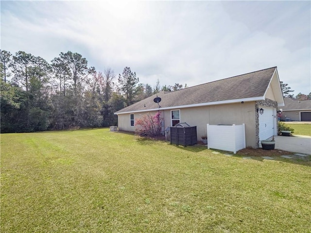 rear view of property featuring a garage, a lawn, and a shingled roof