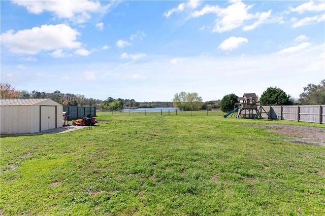 view of yard with an outbuilding, a playground, fence, and a water view