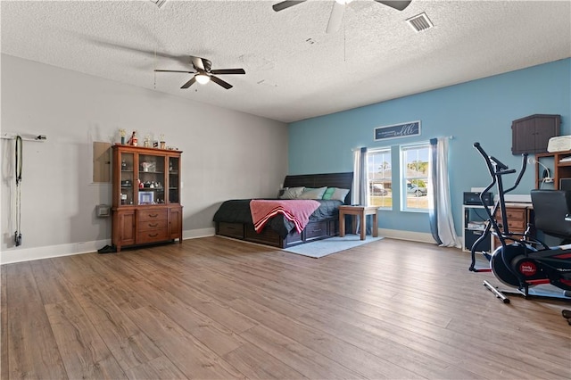 bedroom with a ceiling fan, wood finished floors, visible vents, and a textured ceiling