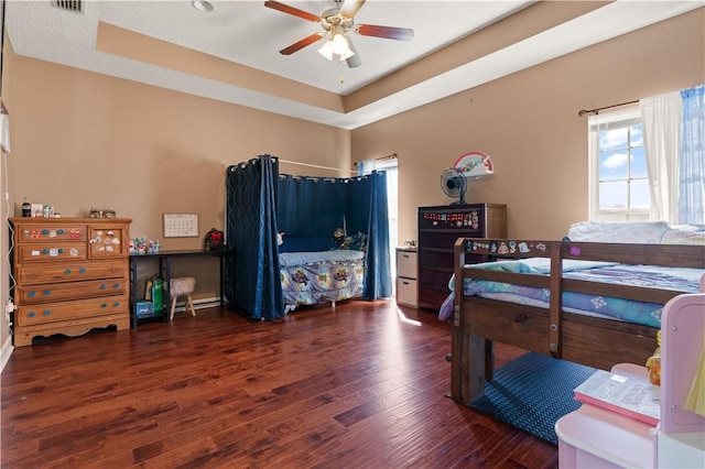 bedroom featuring a ceiling fan, a tray ceiling, wood finished floors, and visible vents