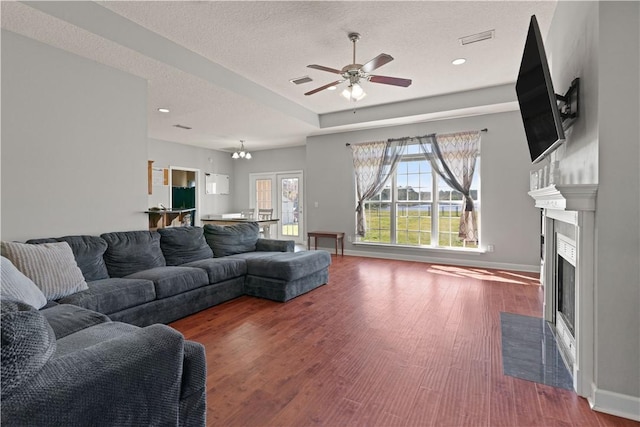 living area featuring a fireplace with flush hearth, wood finished floors, visible vents, and a textured ceiling