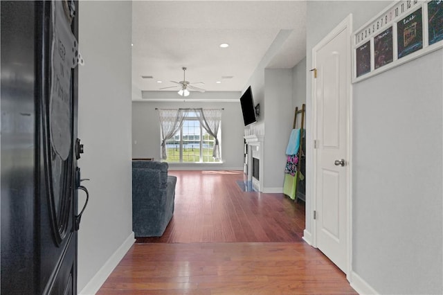 entryway featuring ceiling fan, a fireplace, baseboards, and hardwood / wood-style flooring