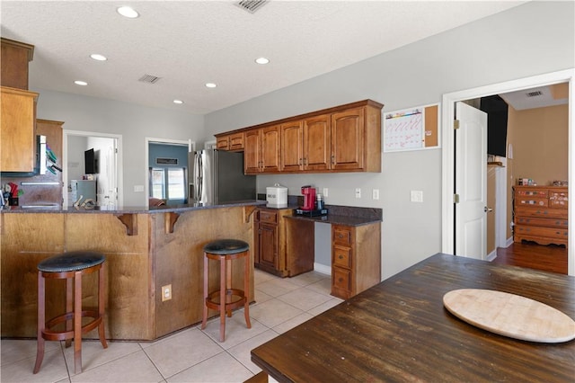 kitchen featuring visible vents, brown cabinets, a kitchen breakfast bar, freestanding refrigerator, and light tile patterned floors