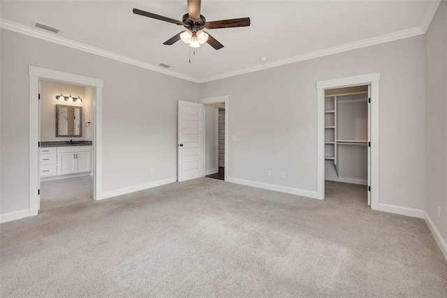 unfurnished bedroom with crown molding, light colored carpet, ensuite bath, and a walk in closet