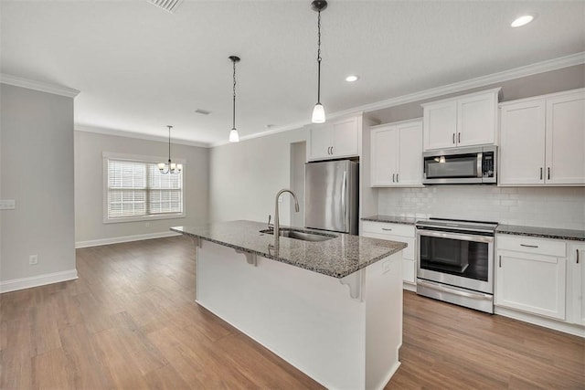 kitchen with pendant lighting, sink, stainless steel appliances, white cabinets, and a center island with sink