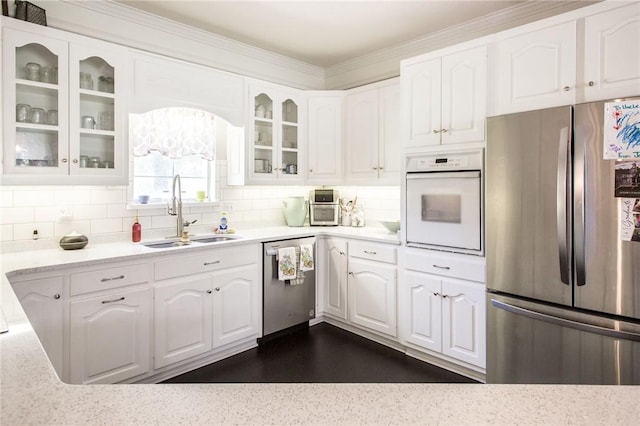 kitchen with appliances with stainless steel finishes, white cabinetry, decorative backsplash, sink, and crown molding