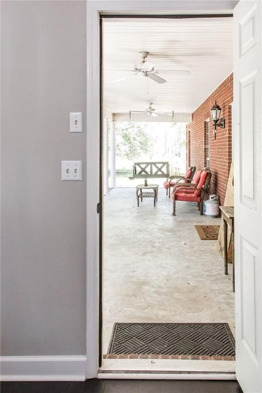 doorway to outside with ceiling fan, brick wall, and concrete flooring