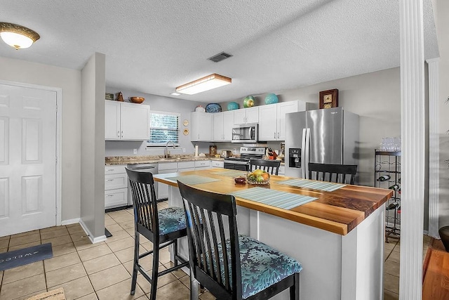 1020 NE Pine Point Ln, Townsend, GA 31331 - kitchen with appliances with stainless steel finishes, light tile patterned floors, white cabinetry, a kitchen bar, and a textured ceiling
