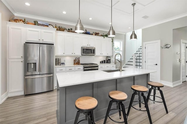 kitchen with a breakfast bar, sink, a center island with sink, appliances with stainless steel finishes, and pendant lighting