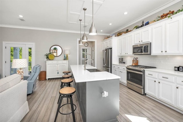 kitchen with appliances with stainless steel finishes, an island with sink, sink, a kitchen breakfast bar, and hanging light fixtures