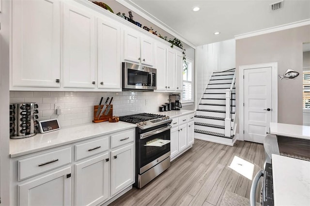 kitchen featuring crown molding, stainless steel appliances, decorative backsplash, and white cabinets