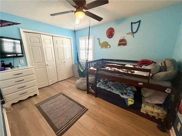 bedroom featuring a textured ceiling, ceiling fan, a closet, and light wood-style floors