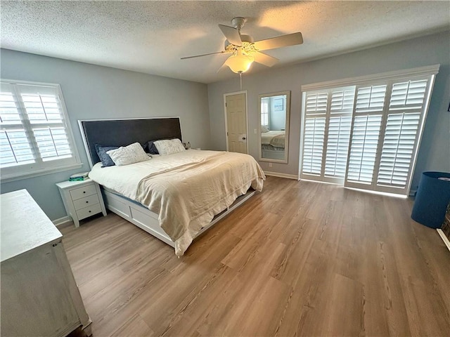 bedroom with light wood-style floors, a textured ceiling, baseboards, and a ceiling fan