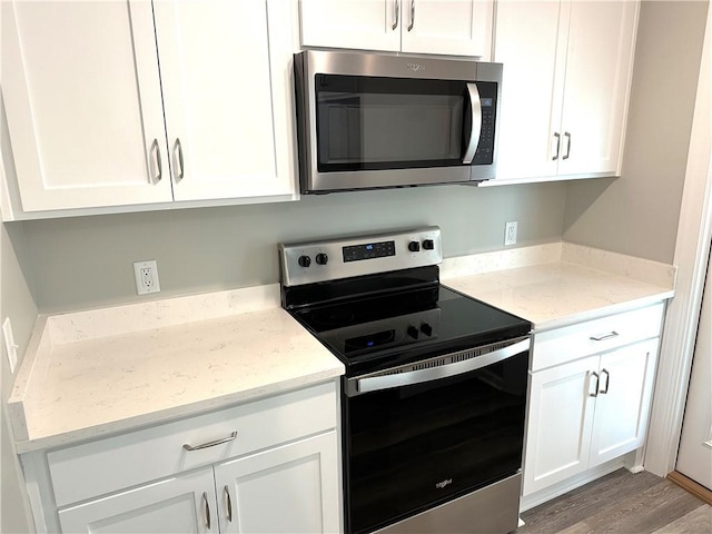 kitchen with white cabinetry, stainless steel appliances, light stone counters, and wood-type flooring