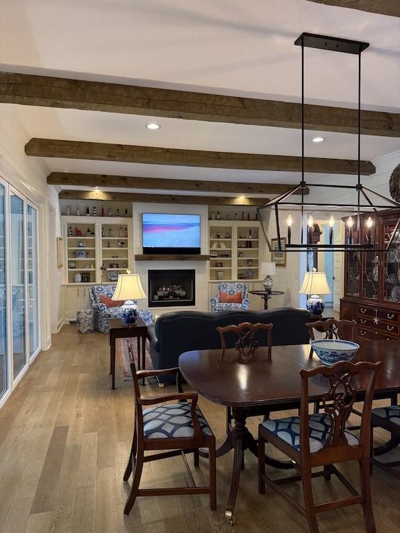dining area featuring an inviting chandelier, wood finished floors, beam ceiling, and built in shelves