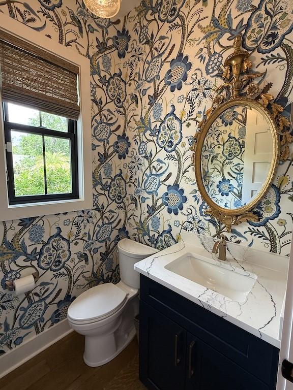 bathroom with toilet, baseboards, vanity, and wallpapered walls