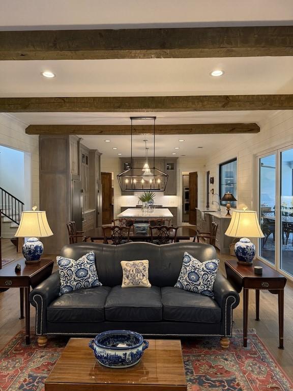 living room with an inviting chandelier, stairs, beamed ceiling, and wood finished floors