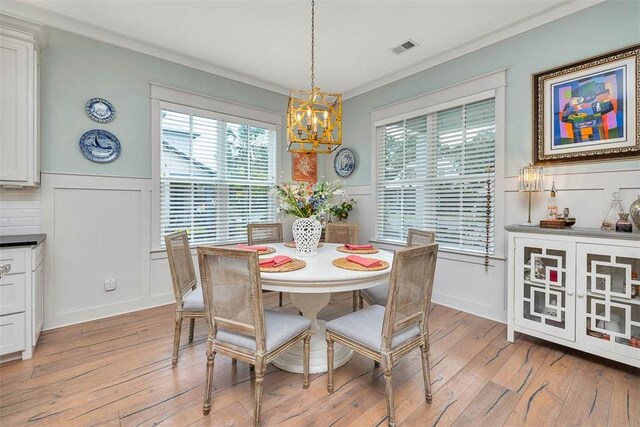 dining area with a chandelier, crown molding, light wood-style flooring, healthy amount of natural light, and wainscoting