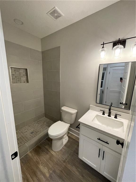 bathroom with wood-type flooring, a textured ceiling, tiled shower, toilet, and vanity