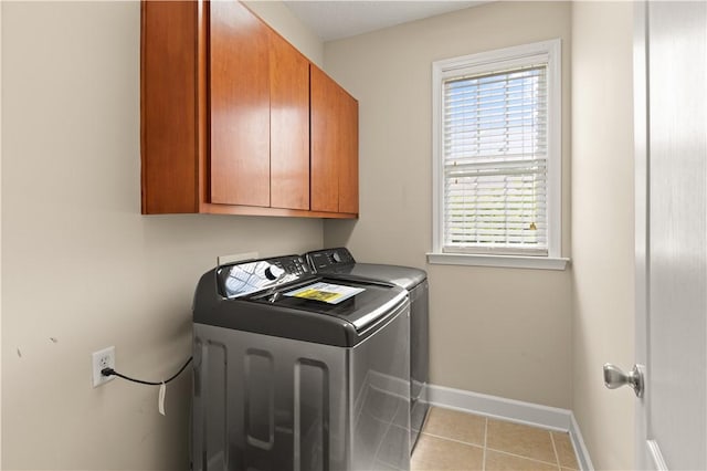 laundry room featuring washing machine and clothes dryer, light tile patterned floors, and cabinets