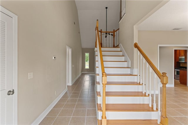 staircase with tile patterned floors and high vaulted ceiling