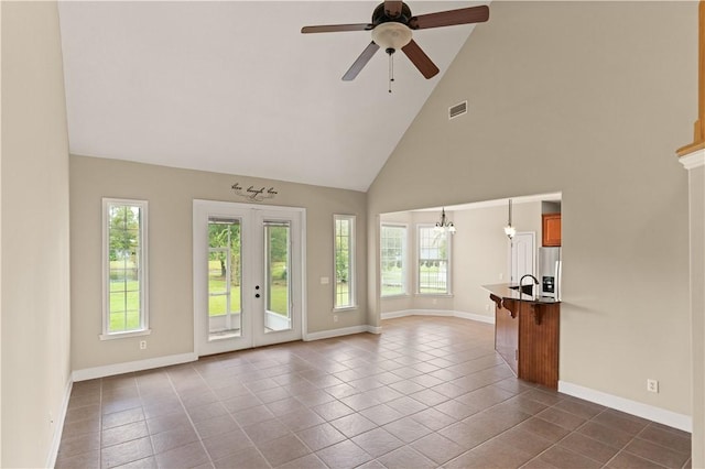 unfurnished living room featuring dark tile patterned flooring, ceiling fan with notable chandelier, high vaulted ceiling, and french doors