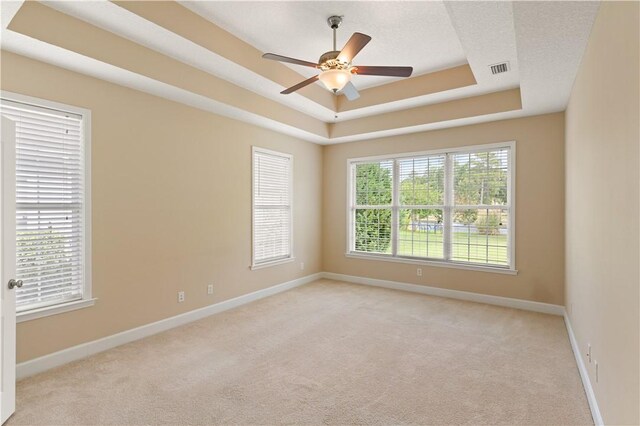 empty room with ceiling fan, light carpet, and a tray ceiling