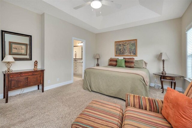 bedroom featuring ceiling fan, connected bathroom, a tray ceiling, and light carpet