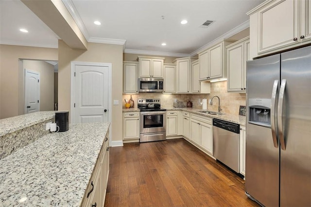 kitchen with appliances with stainless steel finishes, cream cabinets, sink, backsplash, and light stone countertops