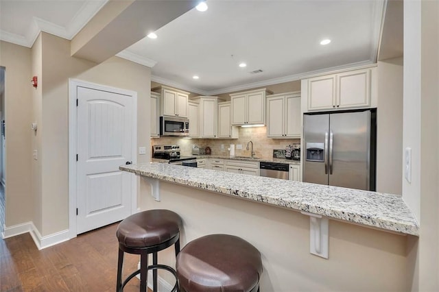 kitchen featuring sink, crown molding, a breakfast bar area, appliances with stainless steel finishes, and light stone counters