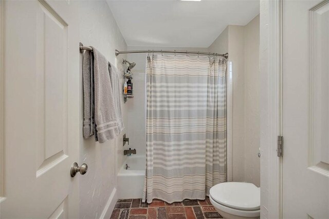 bathroom featuring toilet, shower / tub combo, and brick floor