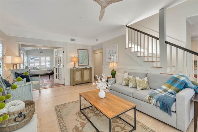 living room with visible vents, a wainscoted wall, light wood-style flooring, and stairs