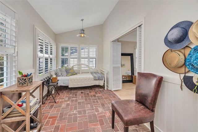 interior space with a decorative wall, a wainscoted wall, lofted ceiling, and brick floor