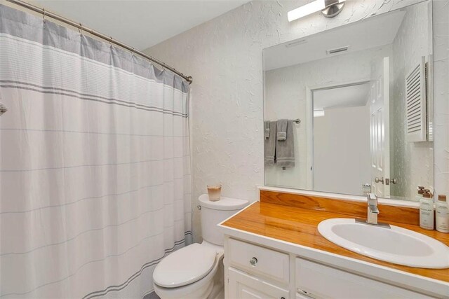 full bathroom with visible vents, toilet, a shower with shower curtain, vanity, and a textured wall