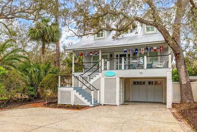 coastal home featuring driveway, covered porch, an attached garage, metal roof, and stairs