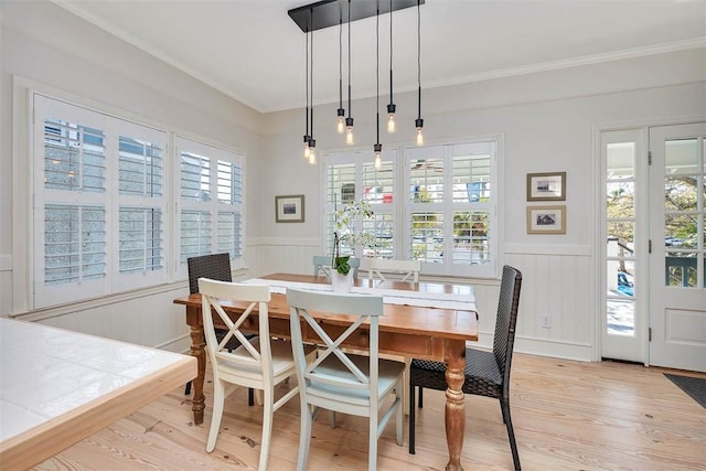 dining space with light wood-type flooring, a wainscoted wall, and ornamental molding