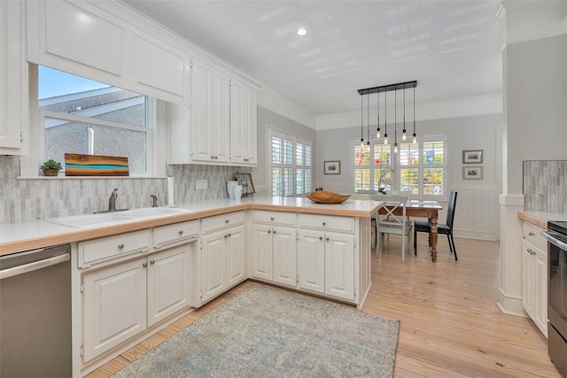 kitchen featuring a peninsula, a sink, stainless steel appliances, light countertops, and light wood-style floors