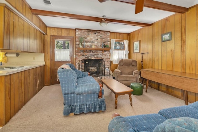 carpeted living room with ceiling fan, wood walls, beamed ceiling, and a brick fireplace