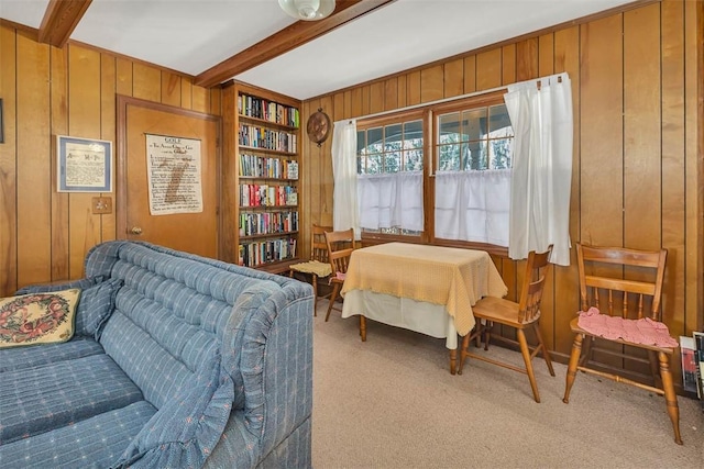 living area with beam ceiling, light colored carpet, and wooden walls