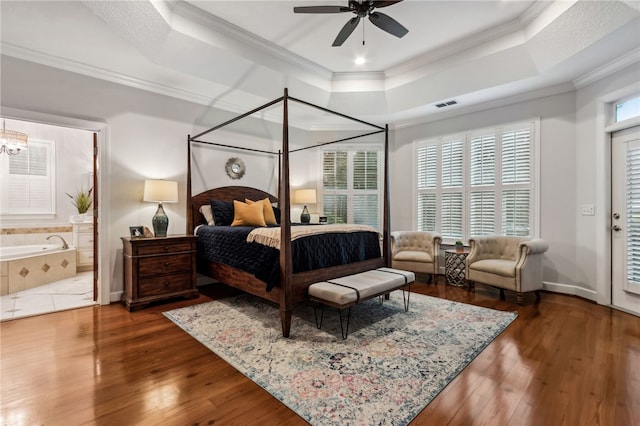 bedroom featuring a tray ceiling, wood-type flooring, visible vents, ornamental molding, and baseboards