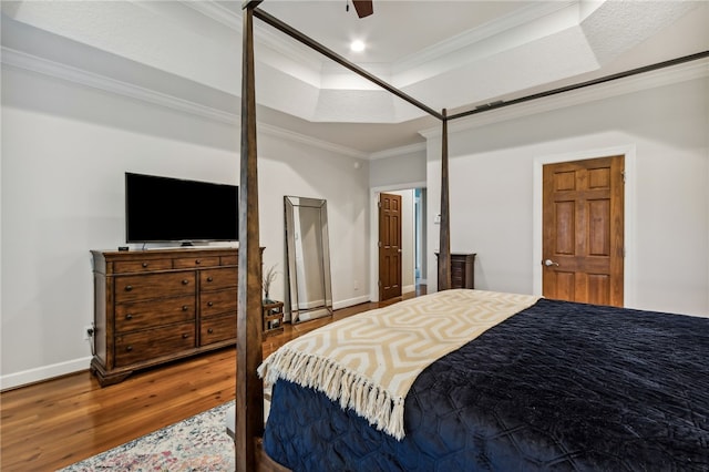 bedroom featuring baseboards, ornamental molding, wood finished floors, a tray ceiling, and recessed lighting