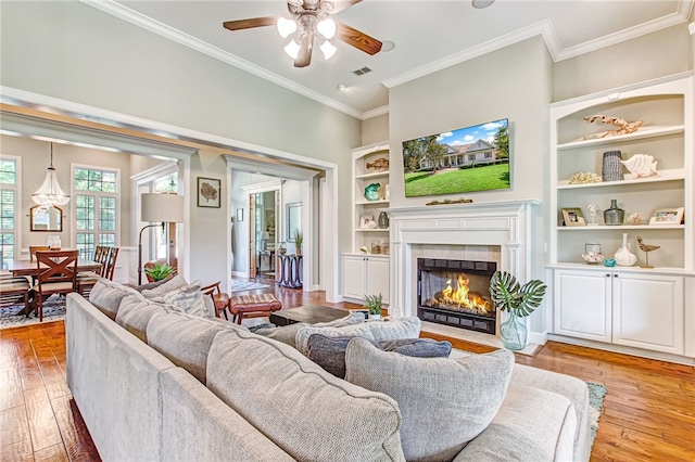 living area featuring light wood-style floors, crown molding, built in shelves, and a tiled fireplace