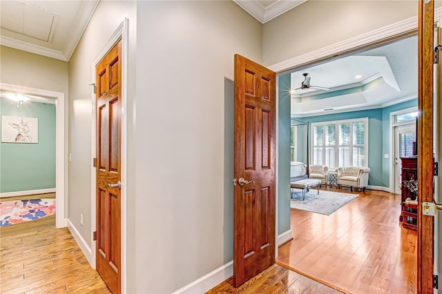 hallway with hardwood / wood-style floors, baseboards, a raised ceiling, and crown molding